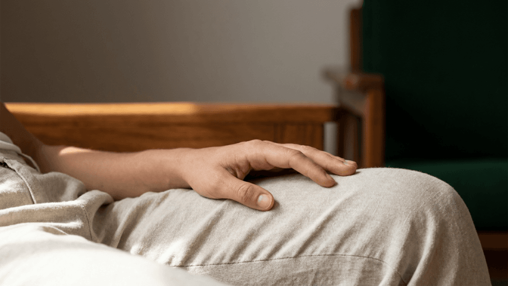 Eine detailreiche Nahaufnahme einer entspannten Hand, die ruhig auf dem hellen Stoff einer beigen Hose liegt, während der obere Bildbereich in sanfter Unschärfe liegt.