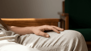 Eine detailreiche Nahaufnahme einer entspannten Hand, die ruhig auf dem hellen Stoff einer beigen Hose liegt, während der obere Bildbereich in sanfter Unschärfe liegt.